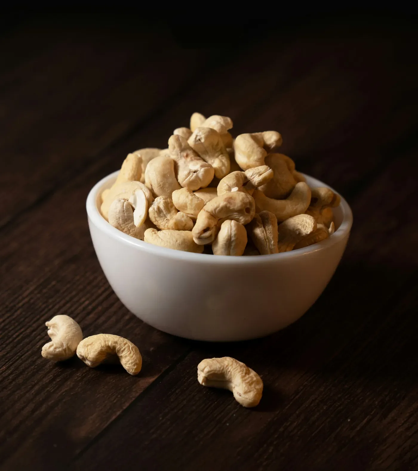 A white bowl of cashews on a dark wooden table