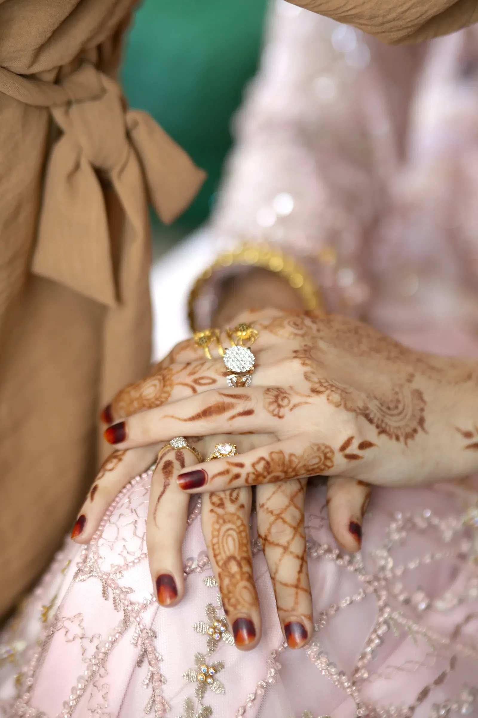 Hands with henna and gold rings resting on a pink embroidered outfit