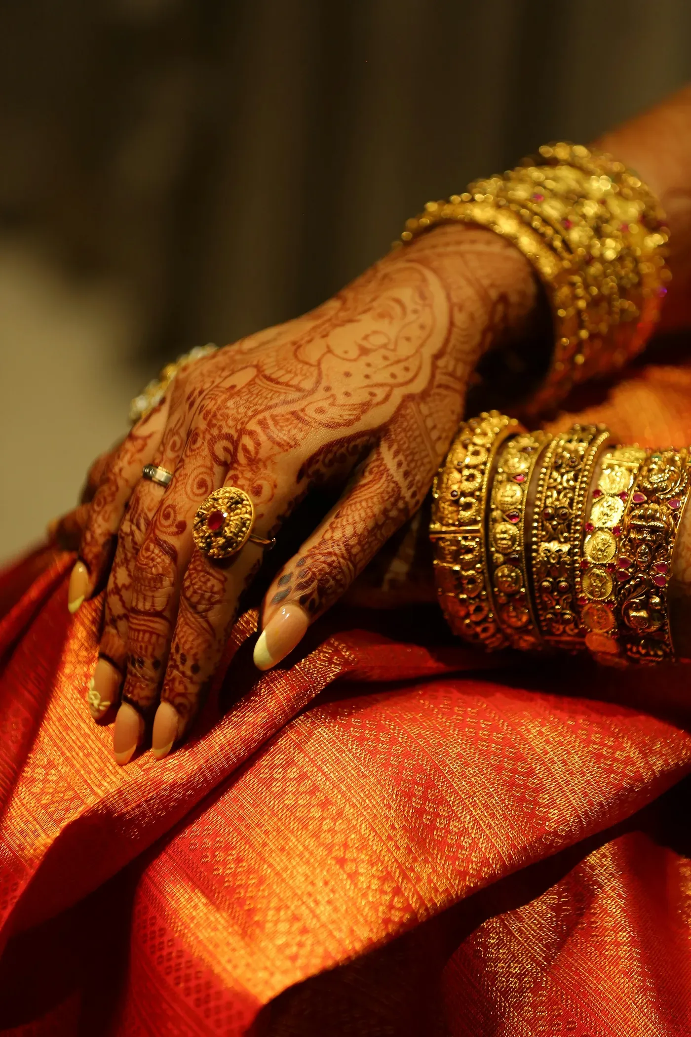 Hands with henna and gold bangles resting on an orange silk saree